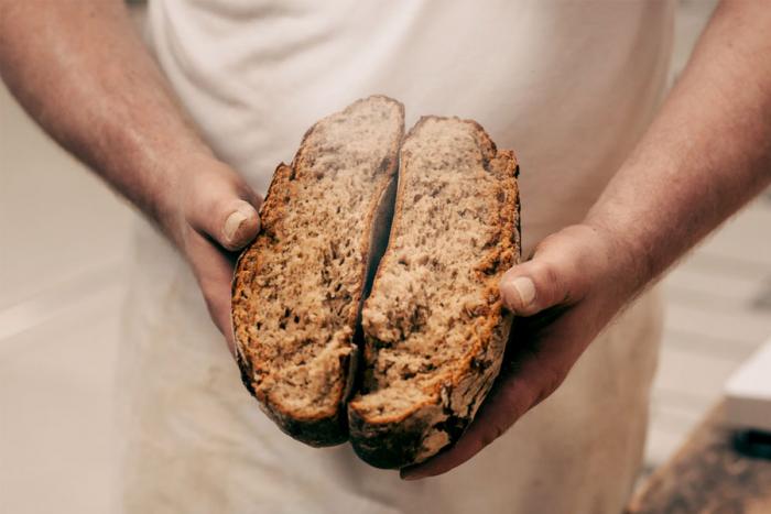 Ein Bäcker bricht ein Brot in zwei Hälften